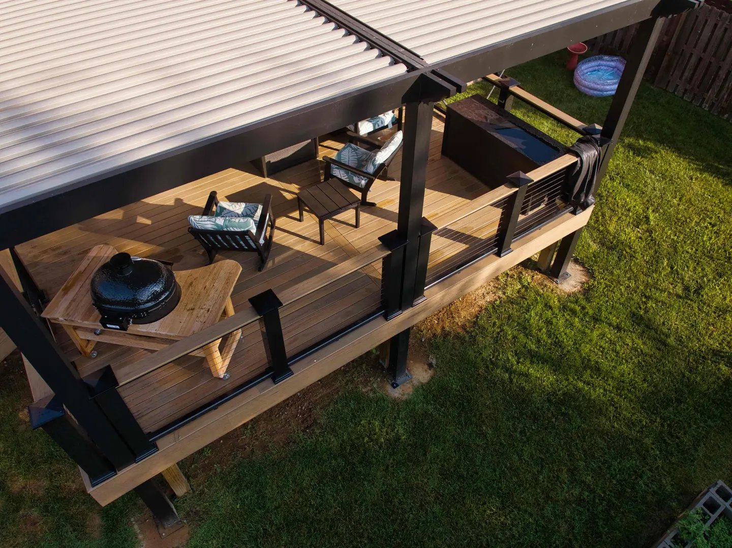 Composite deck under a louvered pergola with a kamado grill station and lounge seating