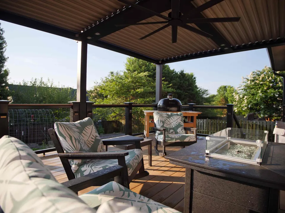 Louvered pergola with a ceiling fan over a deck with a fire table and lounge chairs
