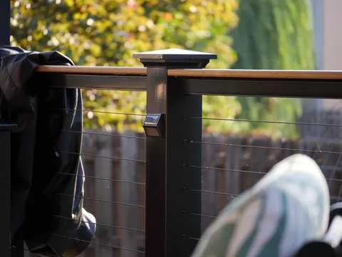 Black deck post with a cap light, stainless cable railing and wood top rail
