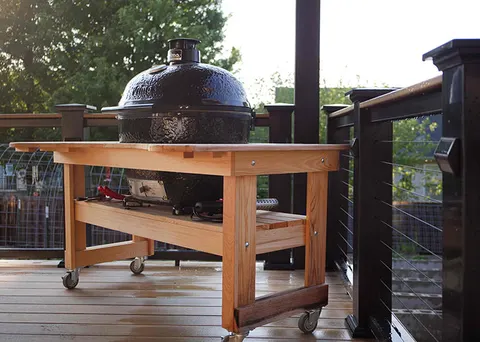 Kamado grill in a cedar cart on a composite deck with stainless cable railing