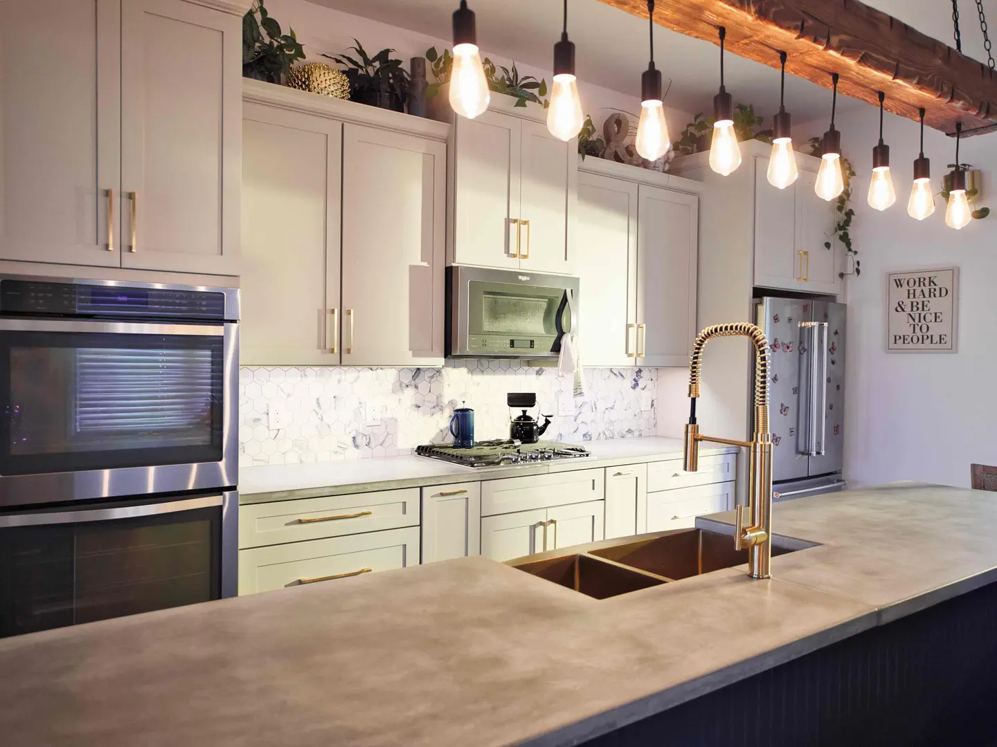 Kitchen with concrete countertops, a copper sink, brass faucet and Edison-bulb pendants hung from a reclaimed beam