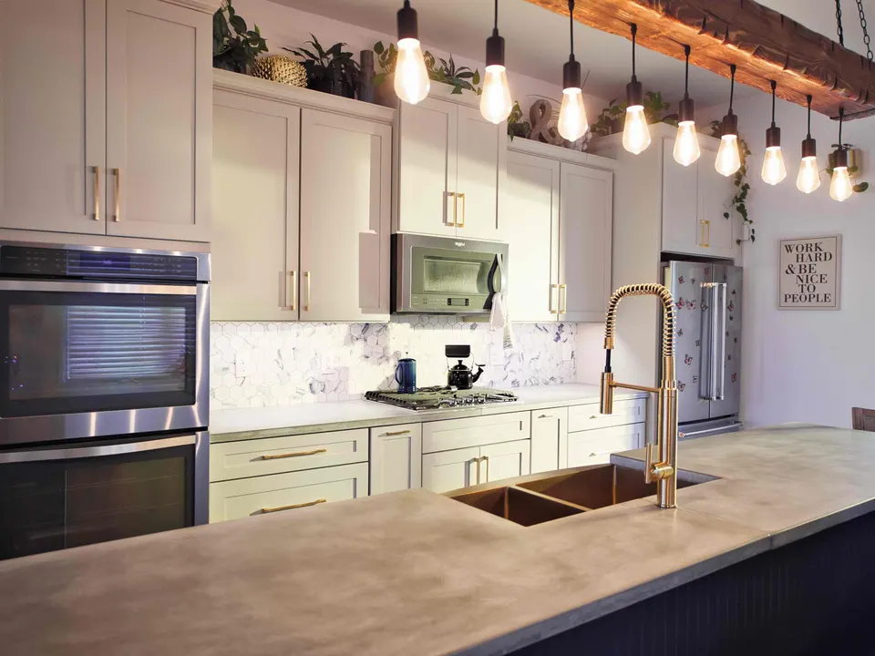 Kitchen with concrete countertops, a copper sink, brass faucet and Edison-bulb pendants hung from a reclaimed beam
