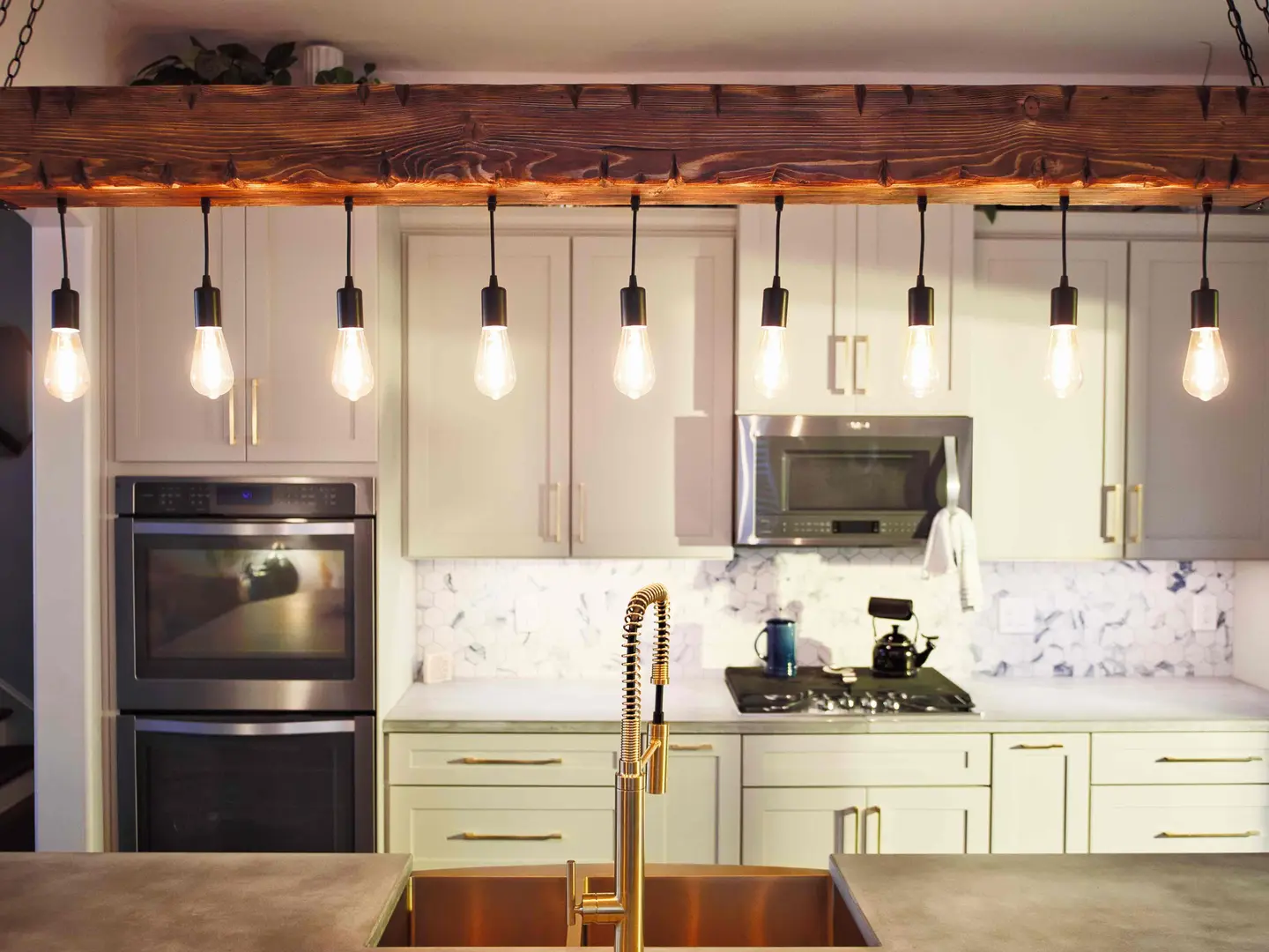 Reclaimed beam with Edison-bulb pendants over a white shaker kitchen with double wall ovens