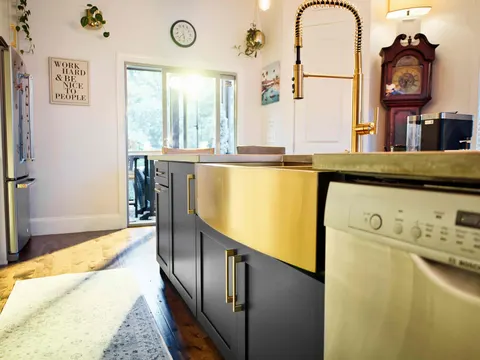 Brass apron-front sink set into a navy island with a spring pull-down faucet